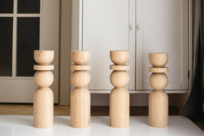 Four wooden candle holders of different heights arranged on a surface with a neutral background.