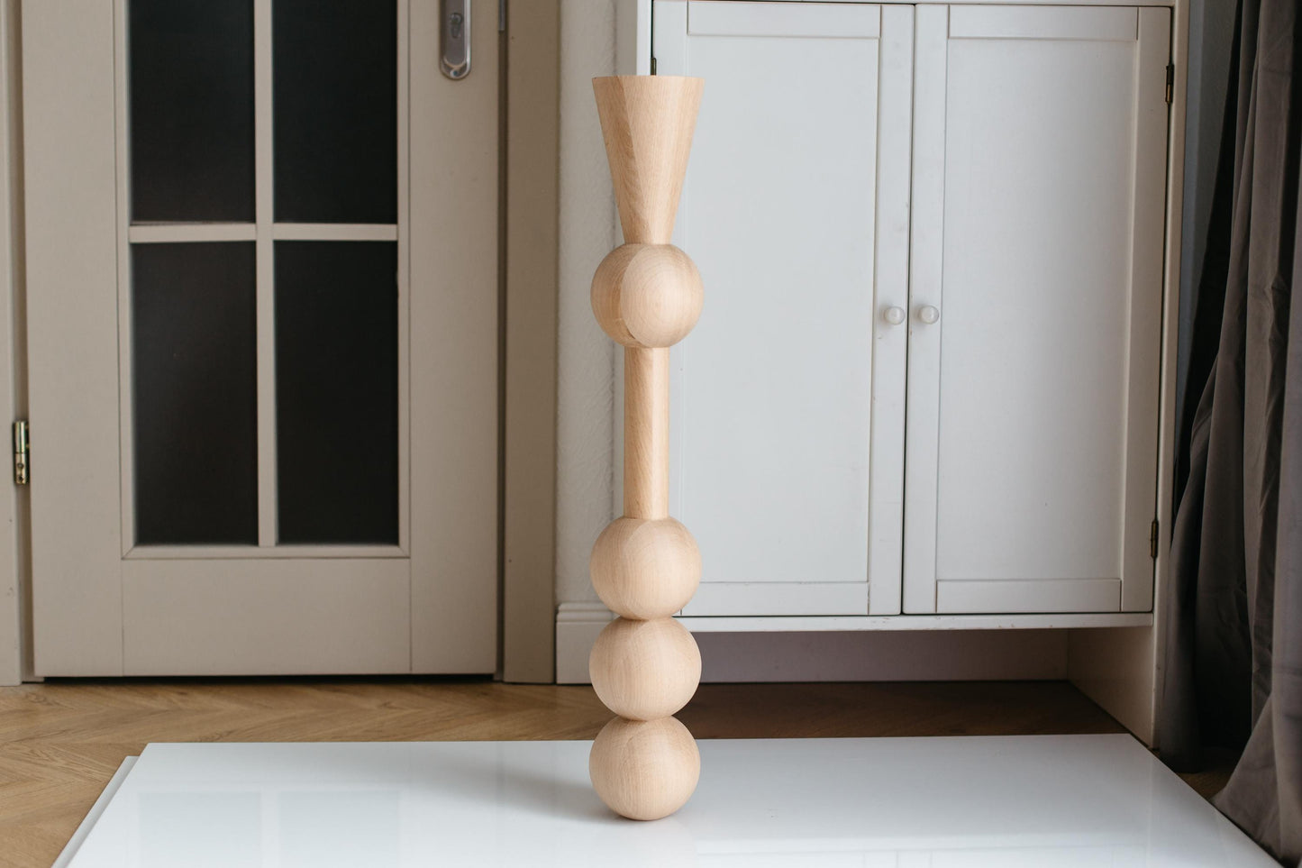 A handmade wooden furniture leg with three spheres, crafted from unfinished raw wood, displayed in an indoor setting.