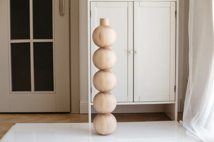 A handmade wooden furniture leg with five spherical shapes, crafted from unfinished raw wood, displayed in an indoor setting.